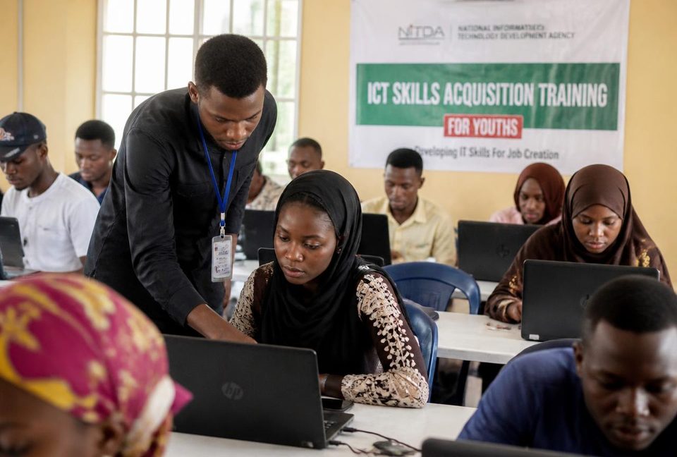 Young trainees learning computer skills on laptops with an instructor in an ICT classroom